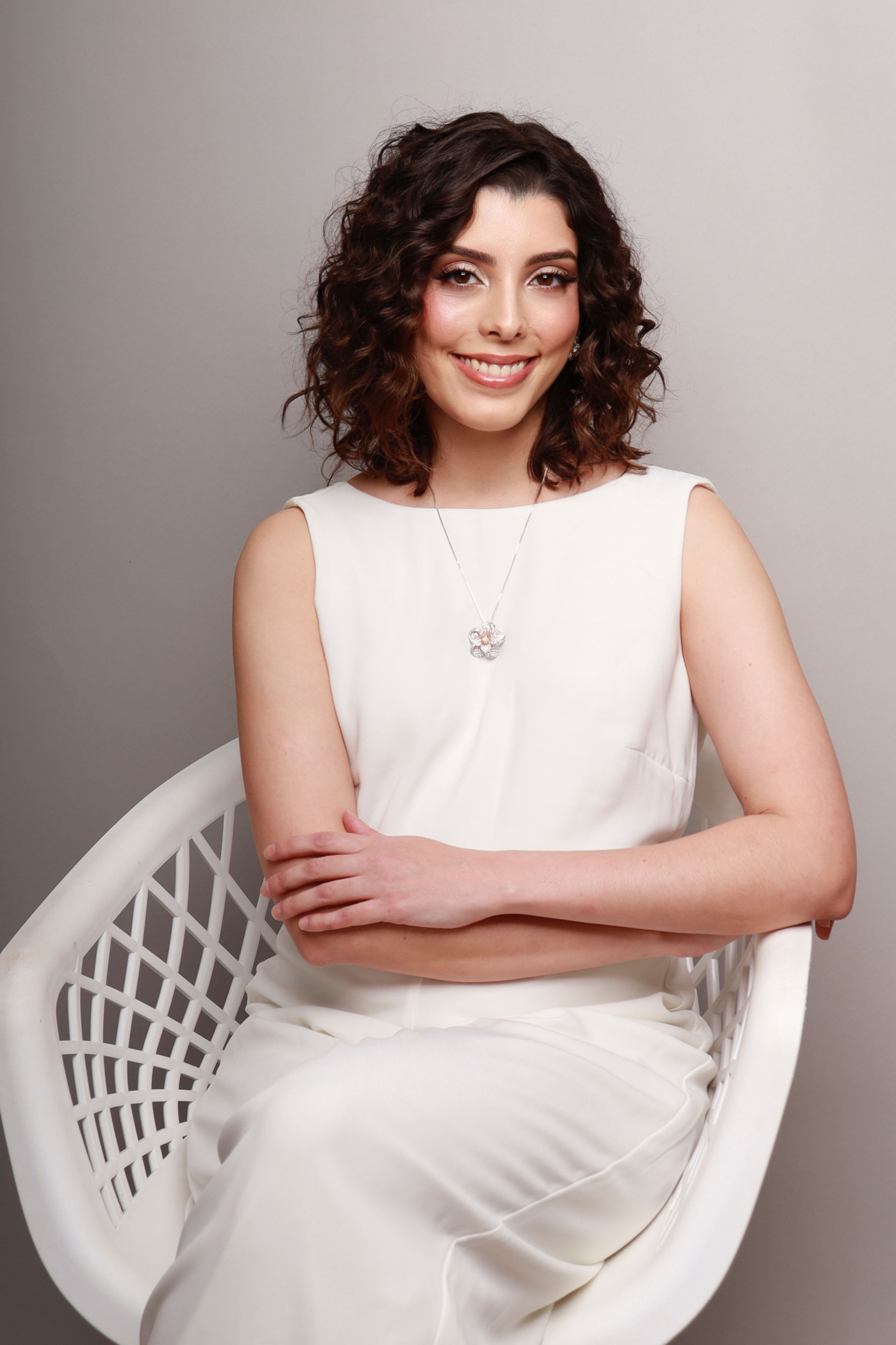 Dra. Isabella Motta sentada em uma cadeira branca sorrindo.